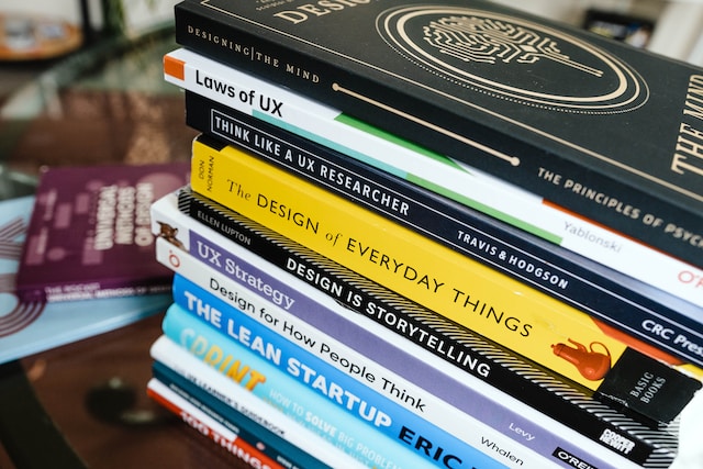  A stack of books about UX design on a brown wooden table. Titles include "Laws of UX" and "The Design of Everyday Things."