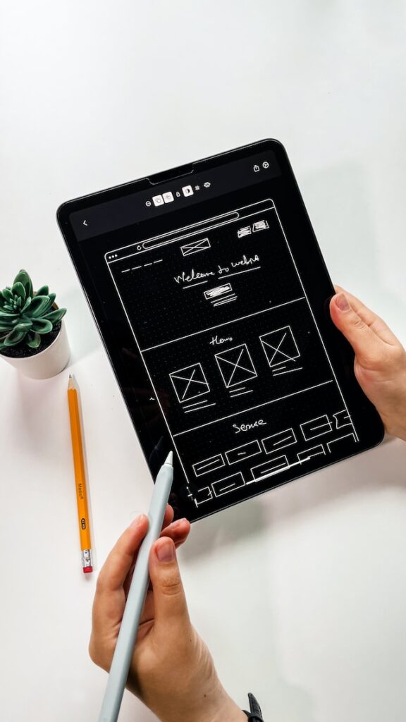 A person holding a black tablet and pen. The tablet has a wireframe sketched on the screen.