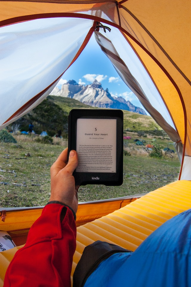 A person holds a turned-on Kindle e-reader inside a tent.