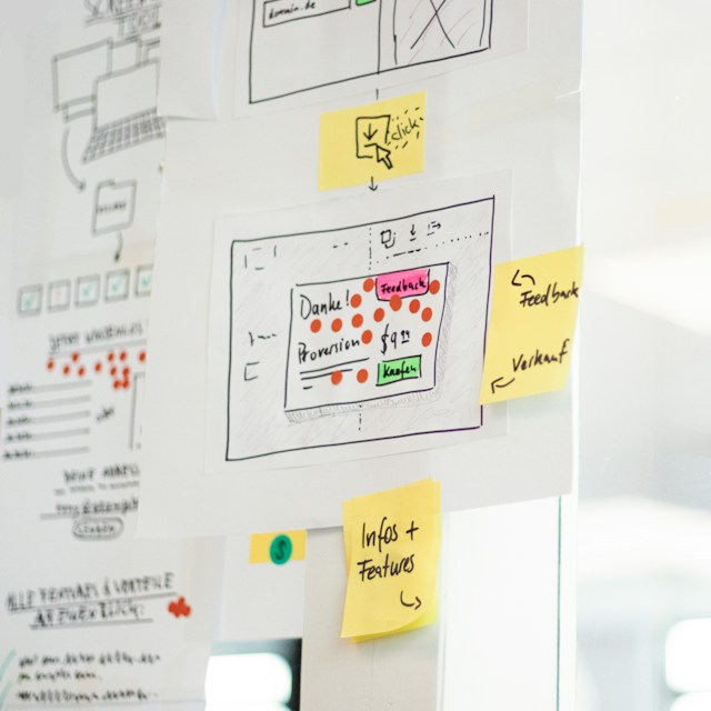 Website wireframe on white paper pinned to a whiteboard, surrounded by post-it notes and annotations.