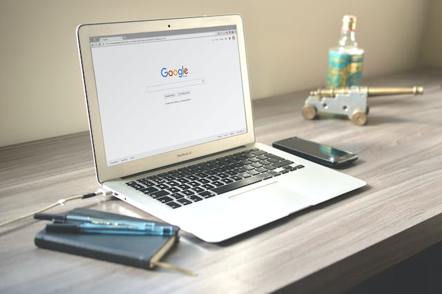 Gray MacBook Air on a wooden table open on the Google homepage.