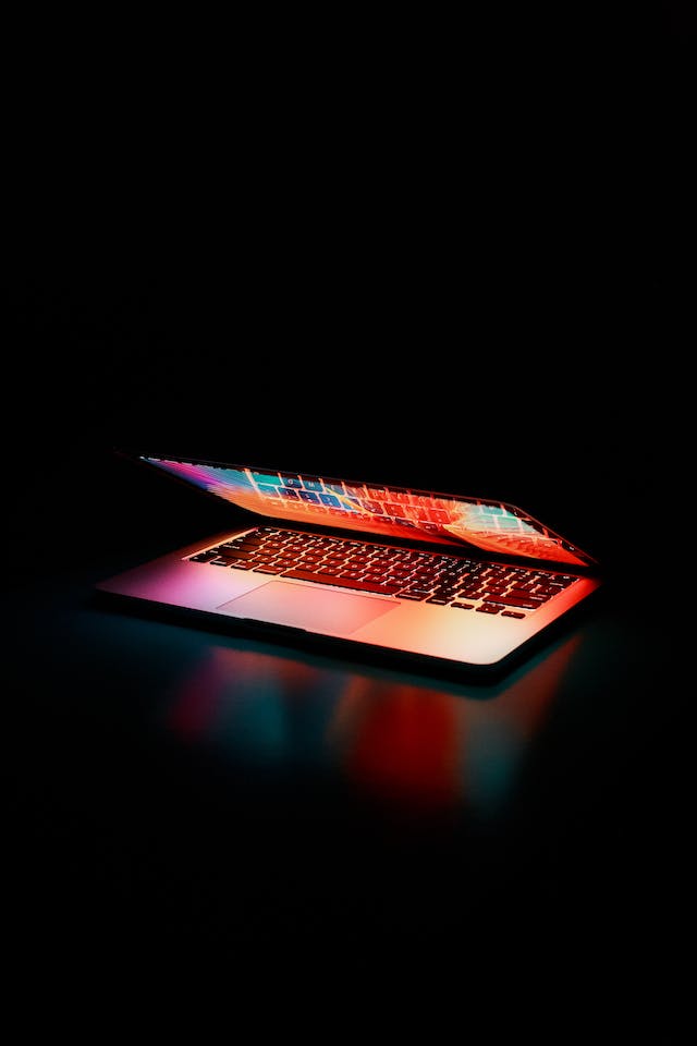 A semi-opened portable computer reflecting the lights of an image onto a black surface in a dark room.