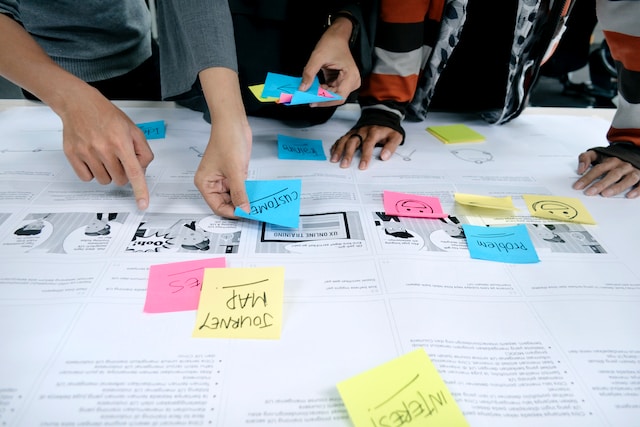 UX researchers add sticky notes to a user journey map while discussing the user flow.
