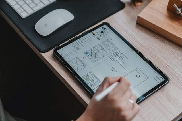 A person draws on an electronic tablet. The drawing displays a series of webpage layouts.