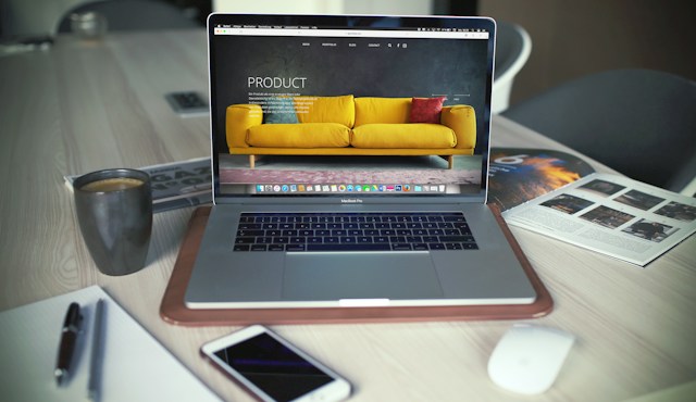A turned-on MacBook is on a wooden table, open on a website homepage.
