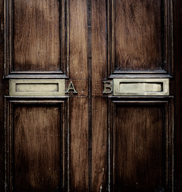 A brown wooden door with two letterboxes labeled with the letter ‘A’ and the letter ‘B’ on it. 