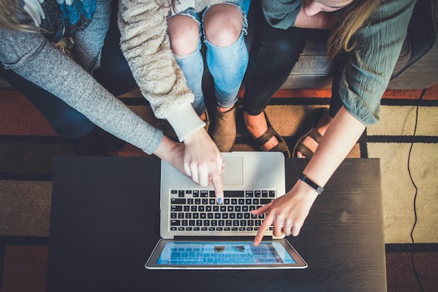 Three people gather around a laptop, pointing at designs on the screen