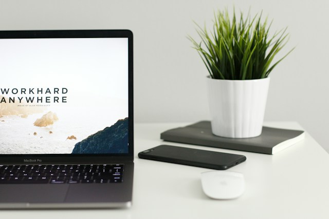 A turned-on Macbook on a white table, open on a website screen that reads "Work hard Anywhere."