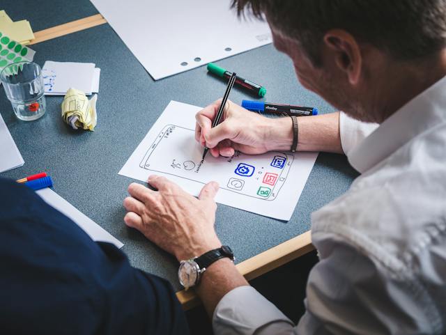 A man draws an illustration of a user interface on a white piece of paper. 