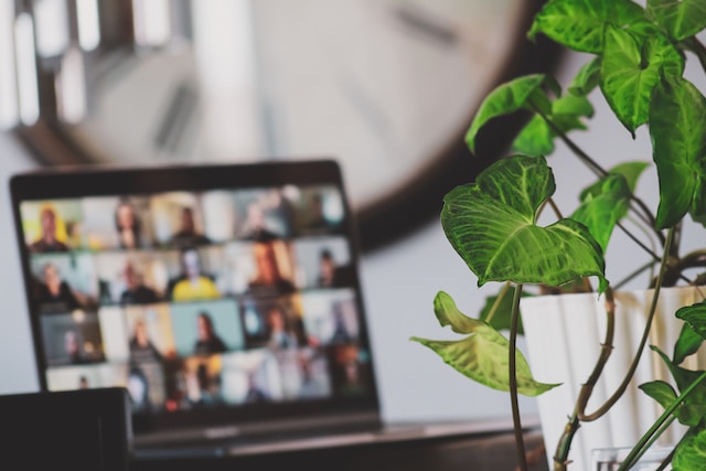 A turned-on laptop is visible but out of focus. The screen appears to show an online course or meeting full of people.