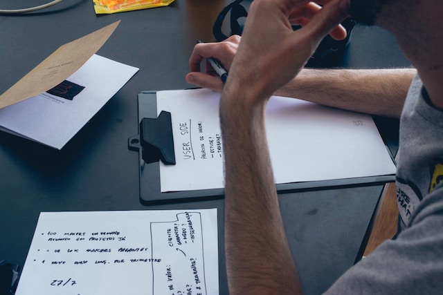 A UX researcher uses a pen to take notes about the user’s perspective on a clipboard and piece of paper.
