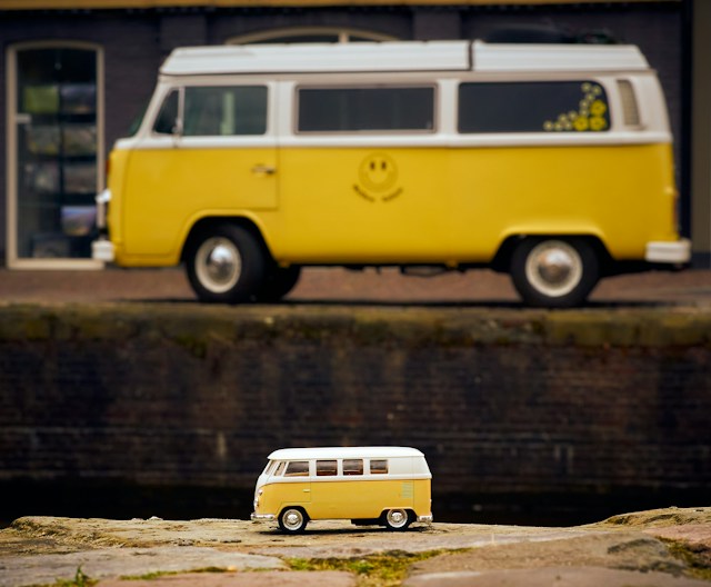 A yellow and white Volkswagen sits in the background. In the foreground sits a smaller model of the car. 
