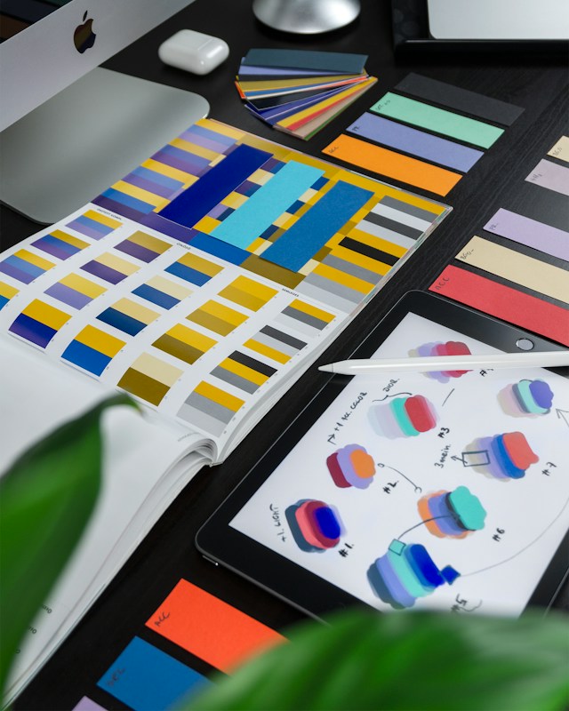 Color swatches on a tablet screen surrounded by open color code books.
