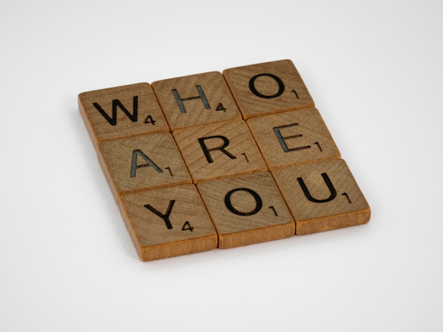 A close-up of Scrabble tiles. The tiles spell out the phrase ‘Who are you?’