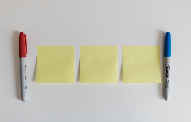 Three blank sticky notes lined up between a red Sharpie and a blue Sharpie.