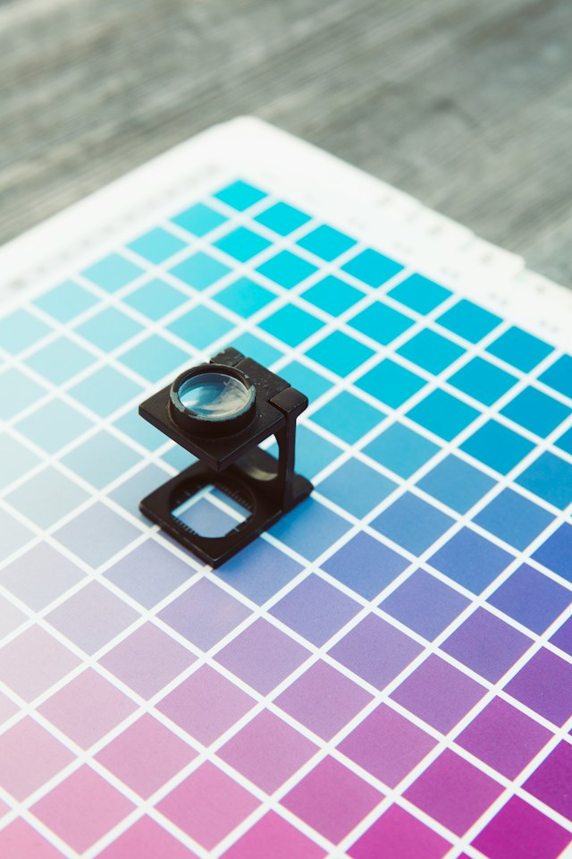 A close-up of a black camera lens on top of a color chart. 

