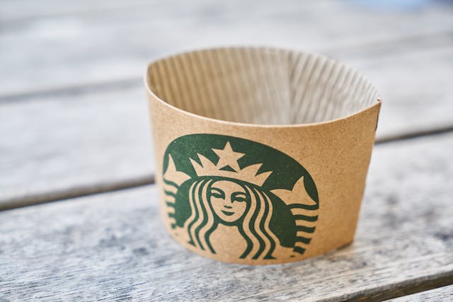A close-up of a brown piece of paper with the Starbucks logo sits on a wooden surface. 
