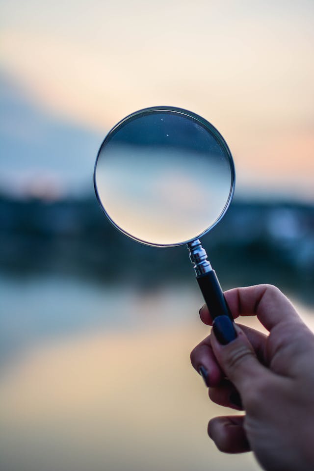 A person holds up a magnifying glass to an obscured background. 
