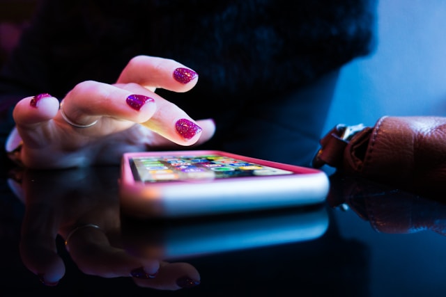 A close-up of a person using a phone resting on a desk, their hand poised as if about to touch the screen.
