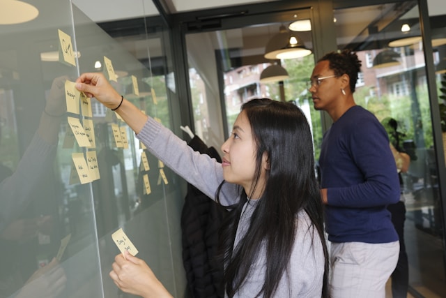 Two people stick sticky notes on a wall.