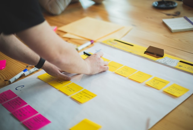 A person writes on sticky notes arranged in lines on white paper.