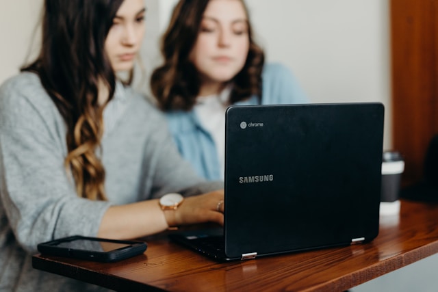 Two women use an open Samsung Chromebook laptop.