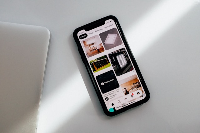 A black iPhone on a white table with the Pinterest main feed on the screen.