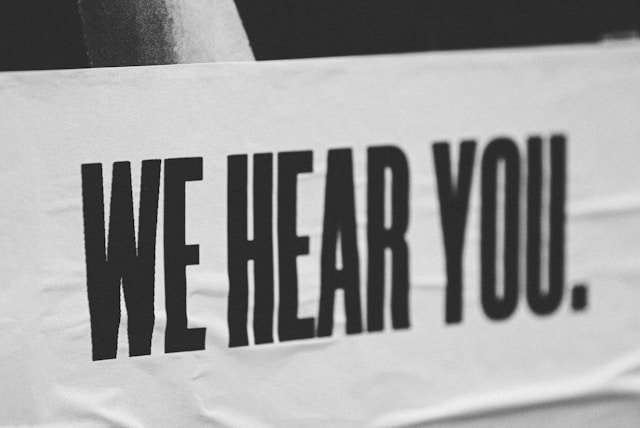 Black and white printed text reading, "We Hear You."
