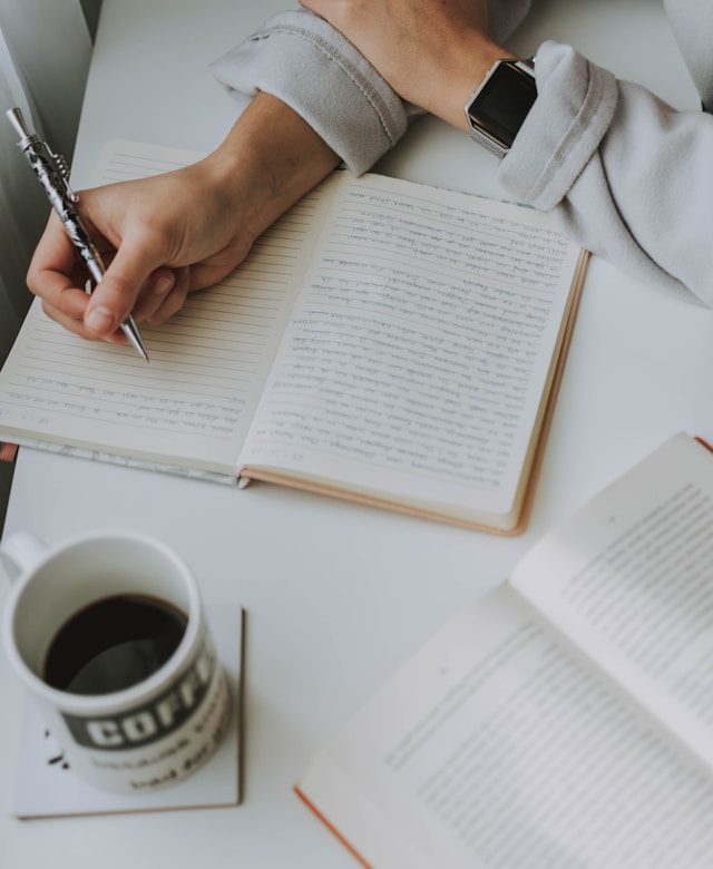 A person writes in their diary on a white table. 
