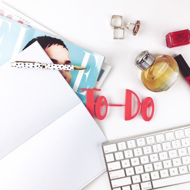 A variety of things are on a desk, including an open notebook and a model of the words 'To-Do.'
