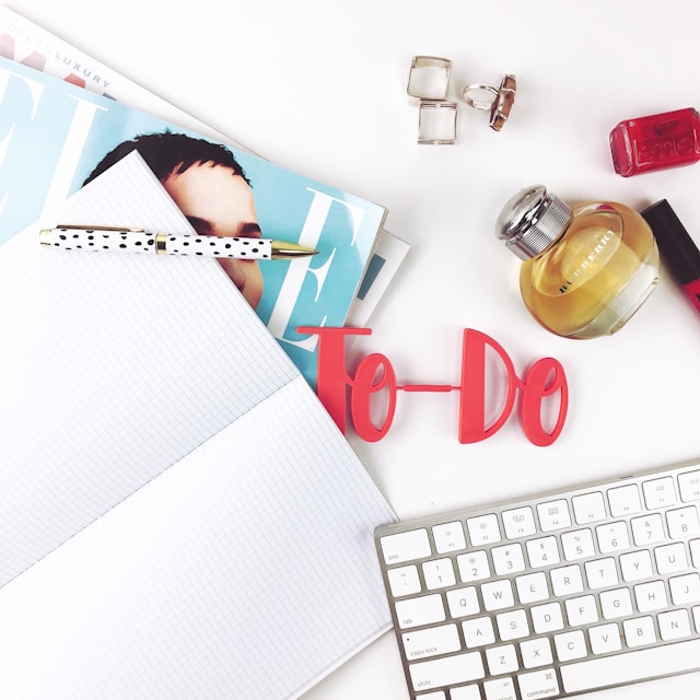 A variety of things are on a desk, including an open notebook and a model of the words 'To-Do.'
