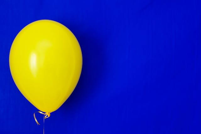 A bright yellow balloon contrasts with a background of dark blue.
