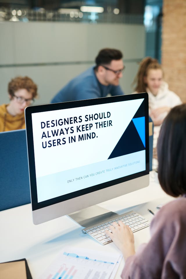 A person sits at their computer. The screen displays the phrase, ‘Designers should always keep their users in mind.’
