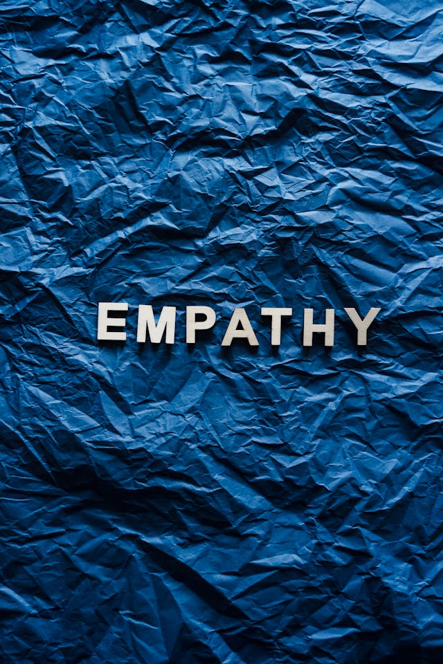 The word ‘Empathy’ appears in a white font on top of a crumpled, blue background. 