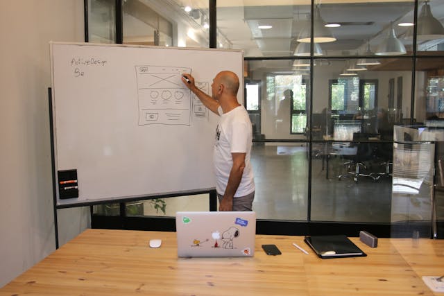 A man stands at a whiteboard, drawing a digital product’s composition. 