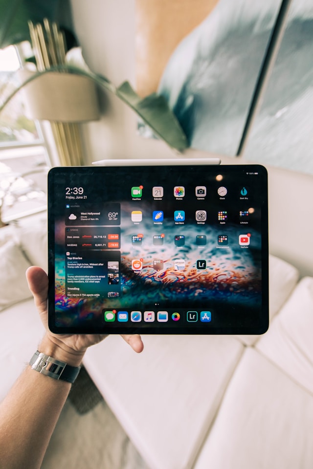 A person holds a turned-on iPad open on the home screen.