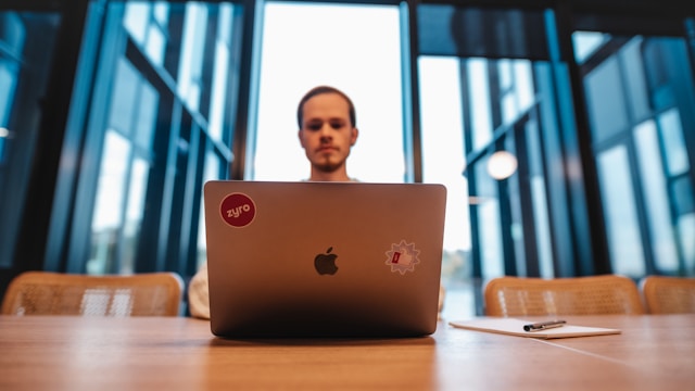 A man sits in front of a Macbook with stickers.
