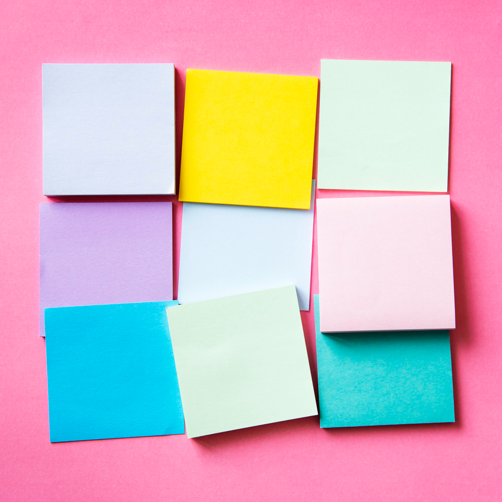 A collection of differently colored sticky notes against a pink background. 
