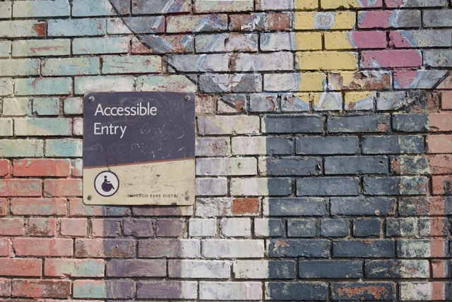 A painted brick wall with a sign depicting a person in a wheelchair. It reads, "Accessible Entry."

