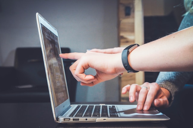 A person uses a laptop while another person points at the screen.