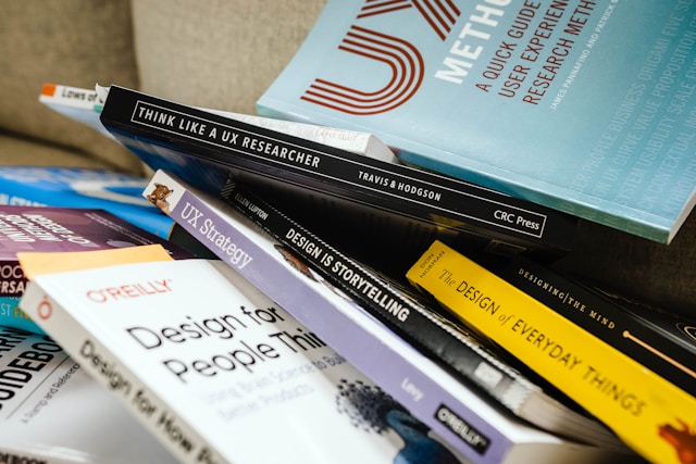 A messy pile of books on UX, including "Think Like a UX Researcher" and "UX Strategy."

