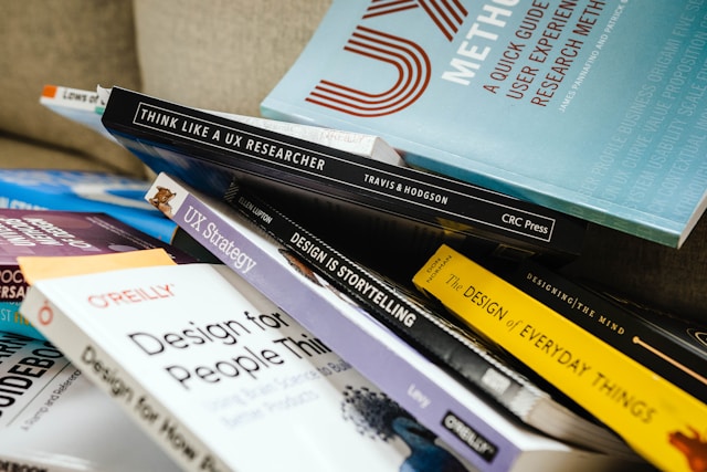 A messy pile of books on UX, including "Think Like a UX Researcher" and "UX Strategy."