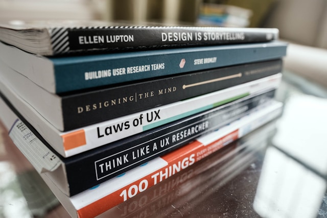 A stack of UX-related books on a table, such as "Laws of UX" and "Think Like a UX Researcher."
