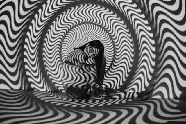 Grayscale image of a woman sitting next to a wall with wavy shadows projected over them. 