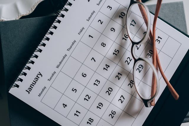 A close-up of a black and white calendar with a pair of brown glasses on top of it. 