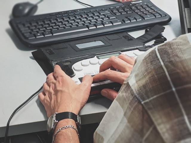 A person uses an alternative keyboard on a desk to operate a computer.
