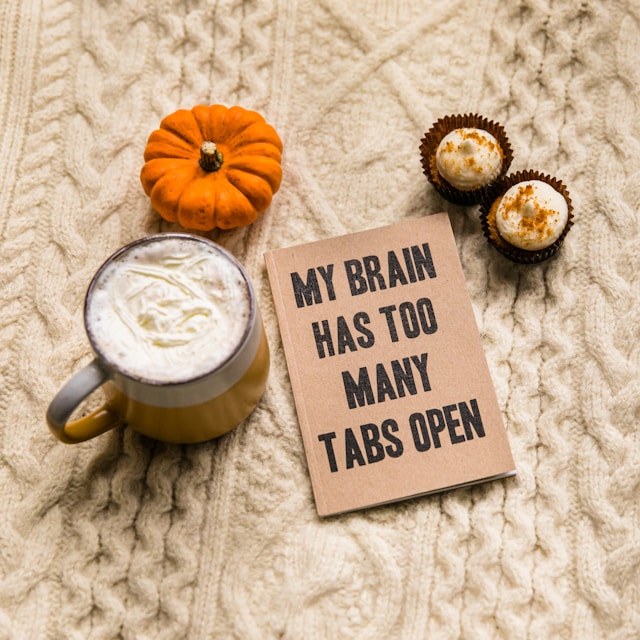A mug of coffee and a notebook on a knitted background. The notebook reads, "My brain has too many tabs open."
