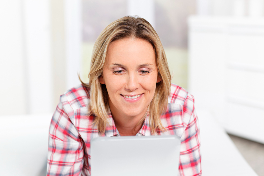 A woman smiles, looking at her white electronic tablet. 