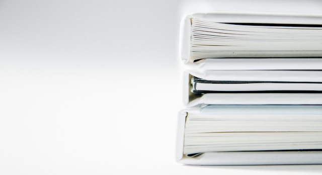 A close-up of a stack of thick white document folders on a white surface. 