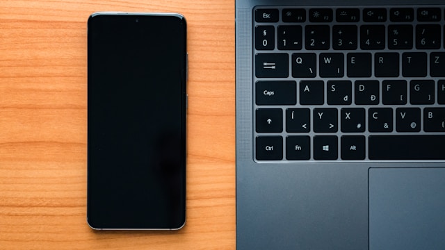 A close-up of a black smartphone next to a black laptop keyboard.